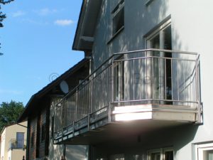 Balkongeländer aus Edelstahl „Standard“-Ausführung: Pfosten und Handlauf aus Edelstahlrohr mit 42,4 mm Durchmesser, waagrecht verlaufende Ober- und Untergurte aus 26,9 mm Edelstahlrohr, Füllung aus senkrechten Edelstahlstäben (Durchmesser 12 mm), mit Blechverkleidung und Regerinne, Befestigung von unten. Rimbach, Kreis Bergstraße, Odenwald